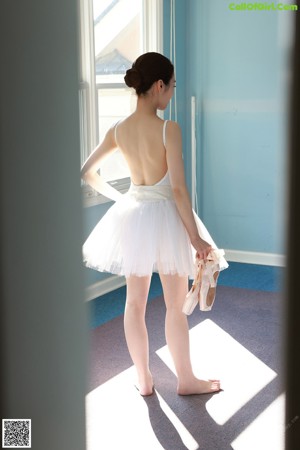 A woman in a white tank top standing by a window.