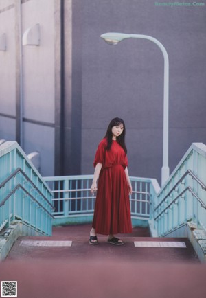 A woman in a red dress standing on a bridge.