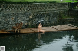 A naked woman holding an umbrella standing on a wooden bridge.