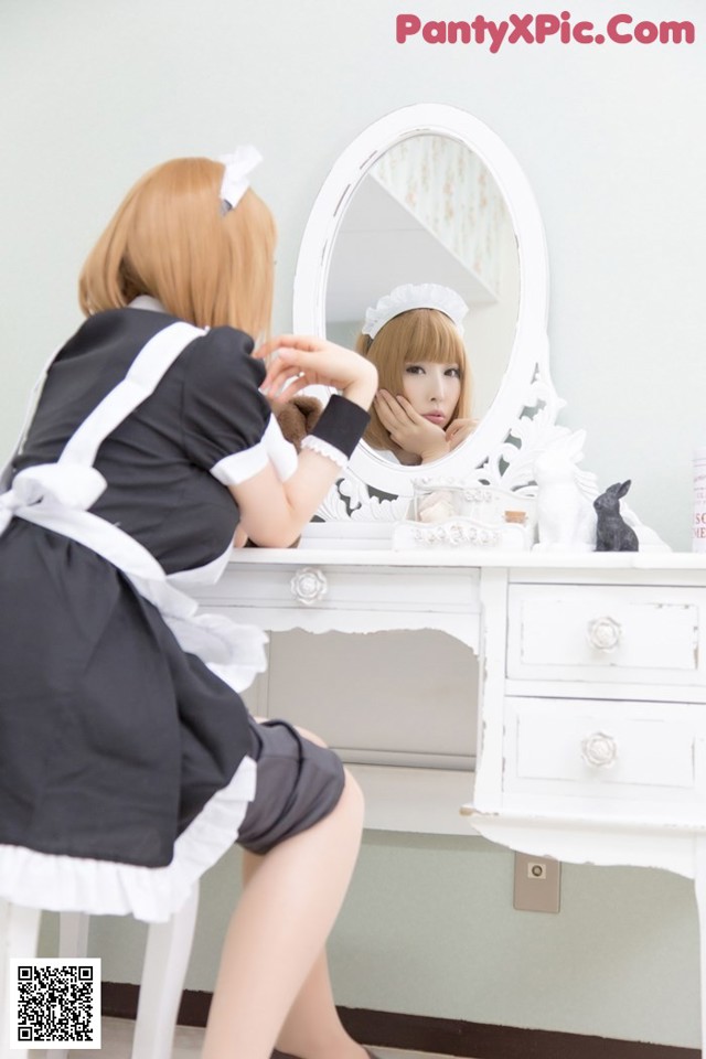 A woman in a maid outfit is looking at herself in the mirror.