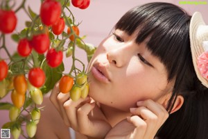 A young woman holding a cherry in front of her mouth.