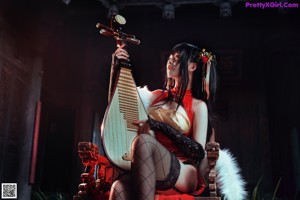 A woman in a red dress sitting on a chair holding a mandolin.
