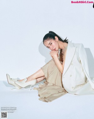 A woman in a beige jacket and white pants posing for a magazine.