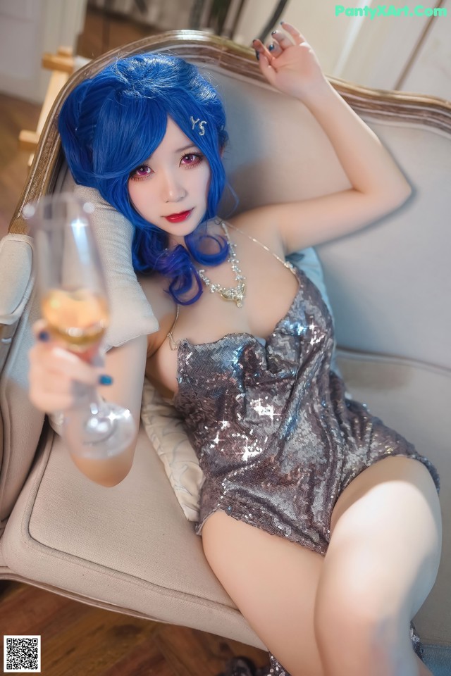 A woman with blue hair sitting on a couch holding a glass of wine.