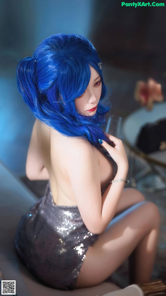 A woman with blue hair sitting on a bed.