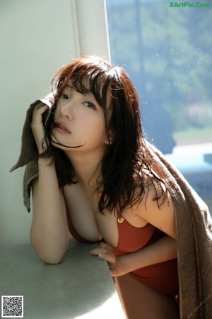 A woman in a red one piece swimsuit laying on a wooden deck by a pool.