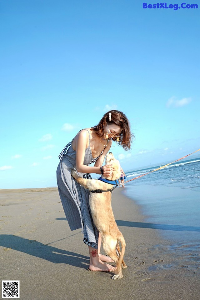 A woman standing on a beach with a dog on a leash.