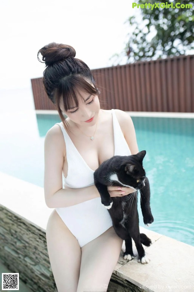 A woman in a white bathing suit holding a black and white cat.