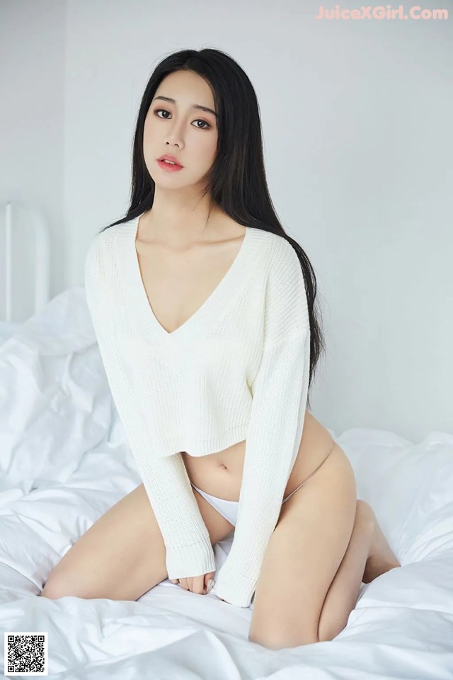 A woman in a white sweater sitting on a bed.