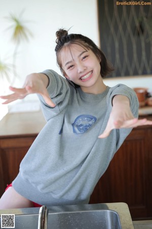 A young woman standing in a kitchen with her arms outstretched.