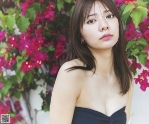 A woman in a blue tank top leaning against a wooden wall.