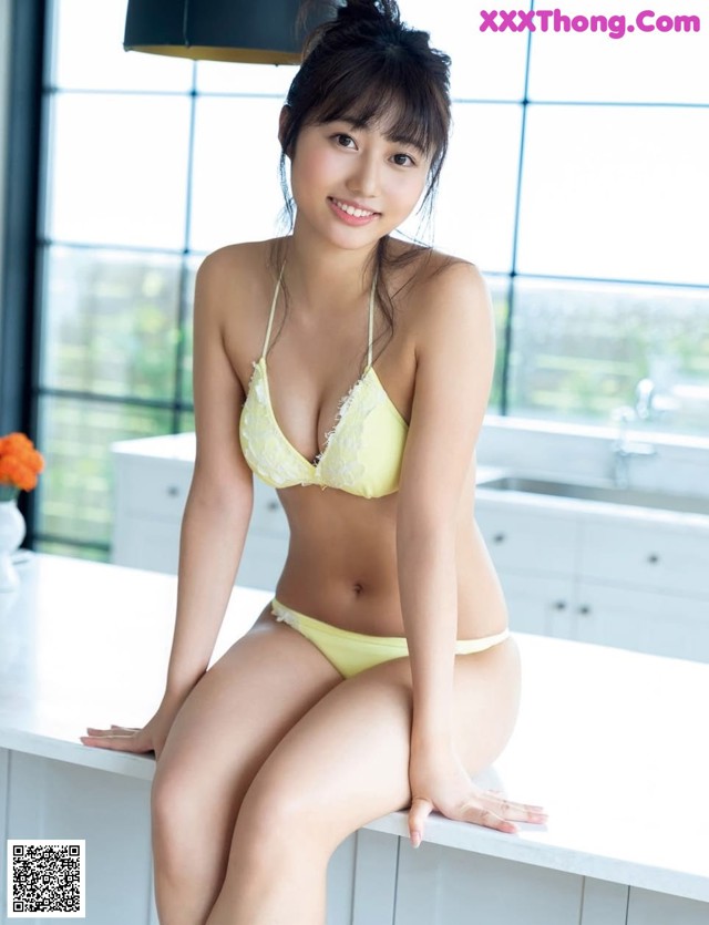 A woman in a yellow bikini sitting on a kitchen counter.