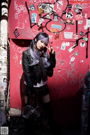 A woman in a black bra top and plaid skirt posing by a window.