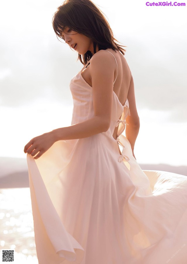 A woman in a white dress standing on the beach.