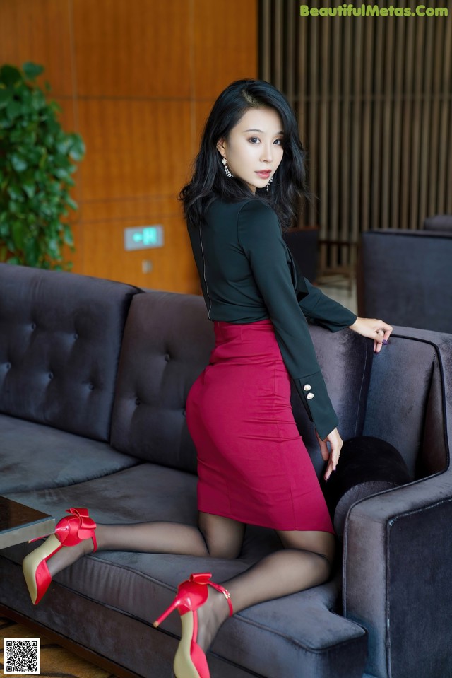 A woman in a red skirt and black shirt sitting on a couch.