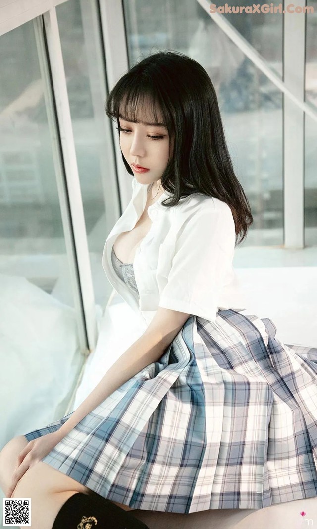 A woman in a plaid skirt sitting on a bed.