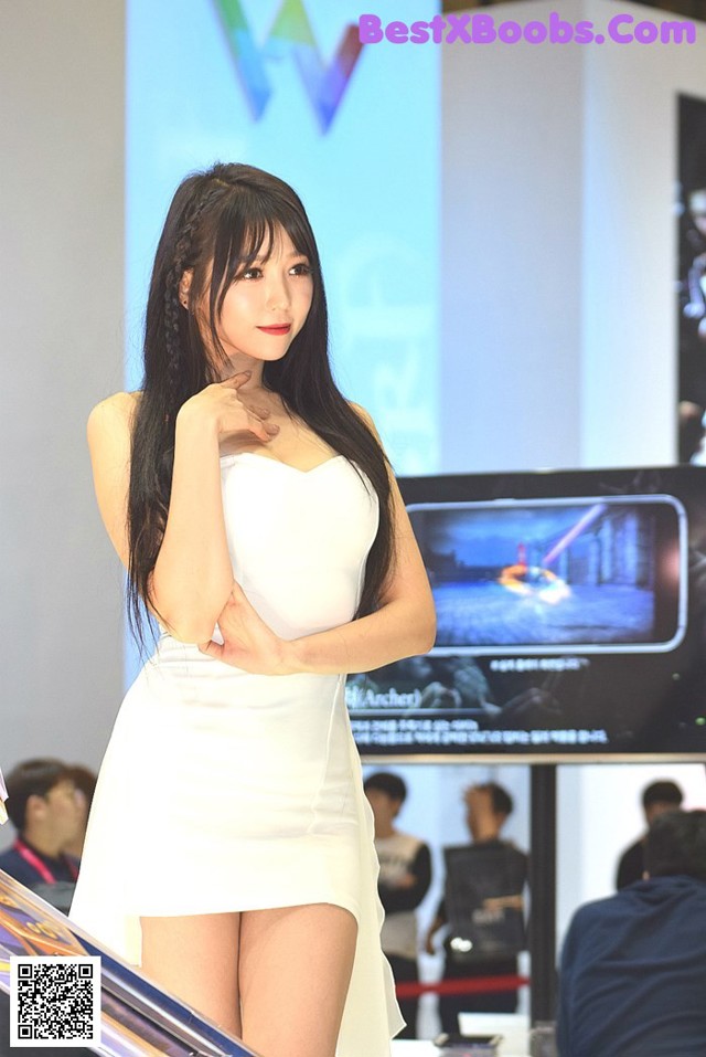 A woman in a white dress standing in front of a television.