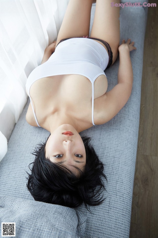 A woman laying on a couch in a white tank top.