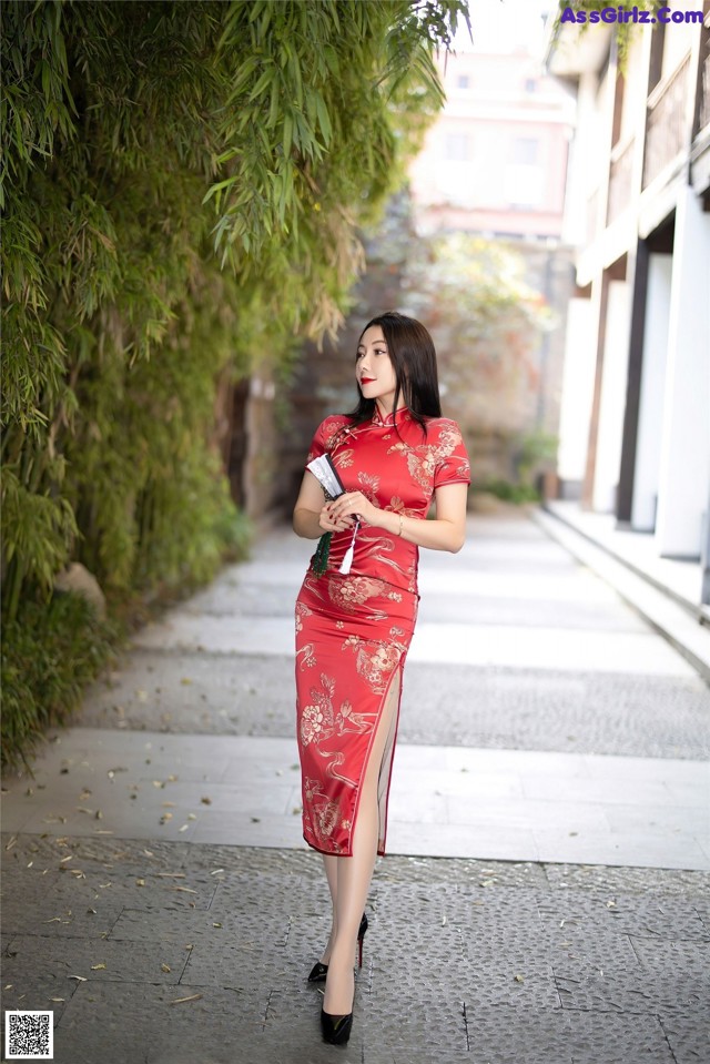 A woman in a red cheongsam standing on a sidewalk.